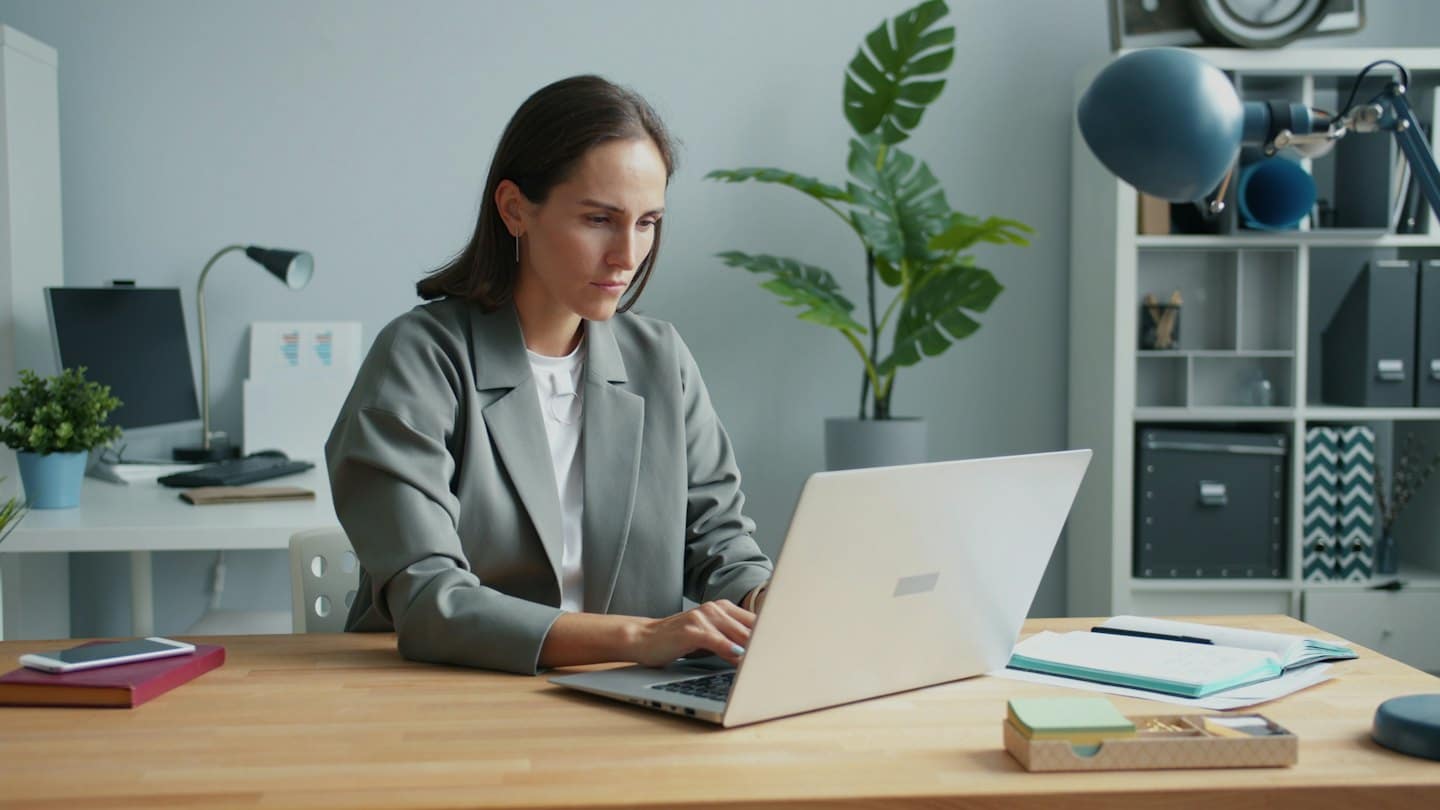 Woman works on her laptop at a desk with plants.